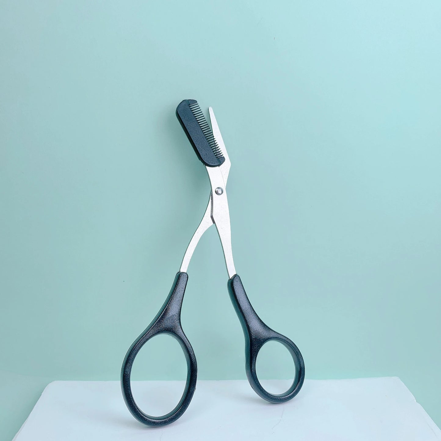Pink stainless steel eyebrow trimming scissors with built-in comb, precise grooming tool for shaping perfect eyebrows.